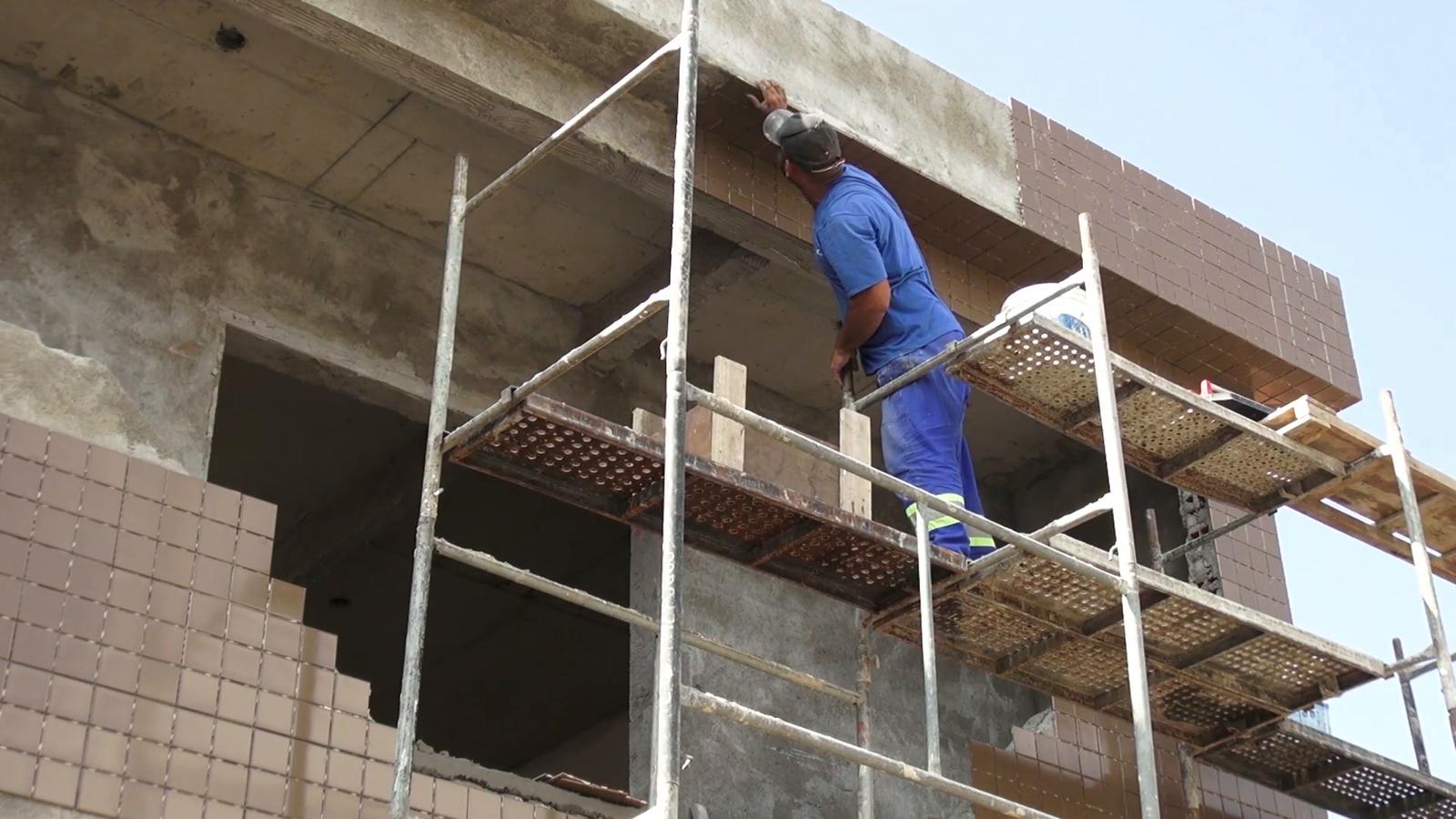 A scaffolder working high on a building under a clear sky.